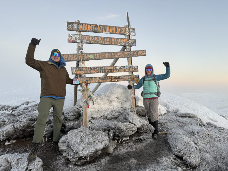 Bergsteiger feiern am Uhuru Peak mit erhobenen Armen auf dem eisigen Gipfel des Kilimanjaro