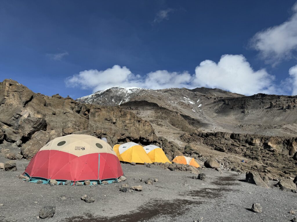 Zelte im Camp am Kilimanjaro mit Wolken und Bergmassiv im Hintergrund