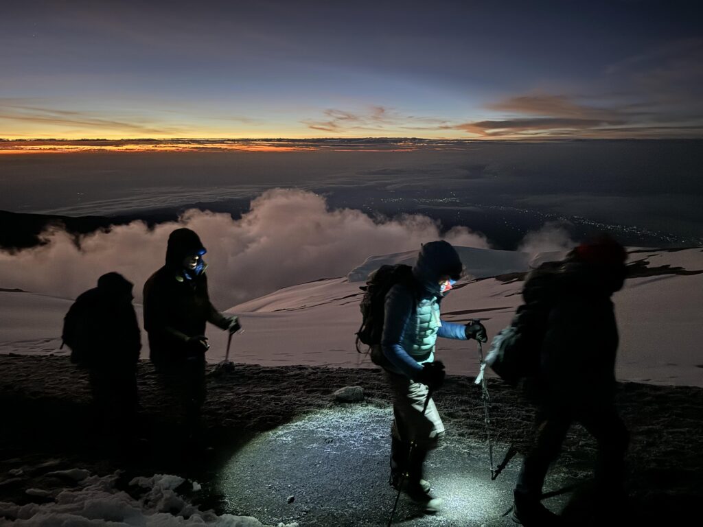 Bergsteiger mit Stirnlampen und Wanderstöcken beim Aufstieg am Kilimanjaro im Sonnenaufgang