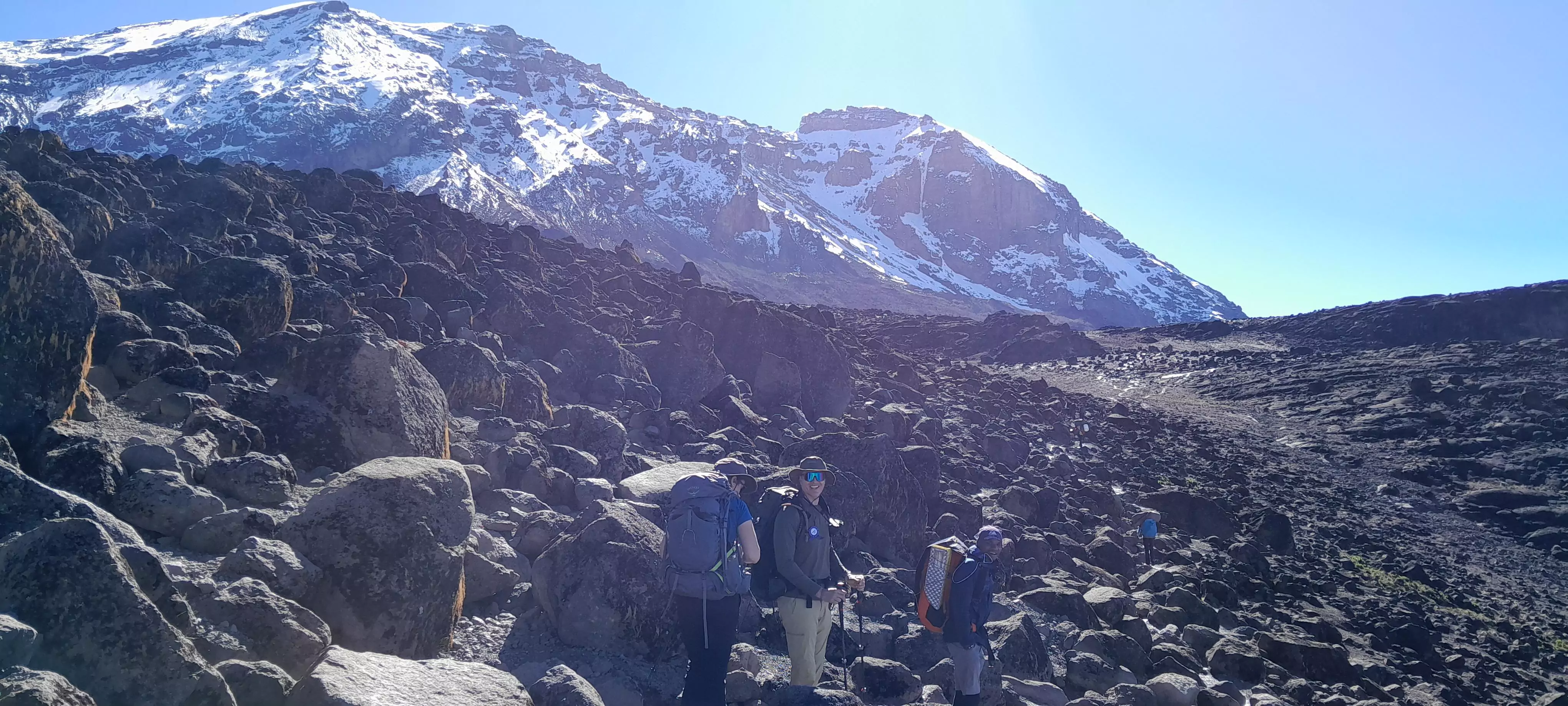 Trekker auf Geröll mit Blick auf den Gipfel des Kilimandscharo