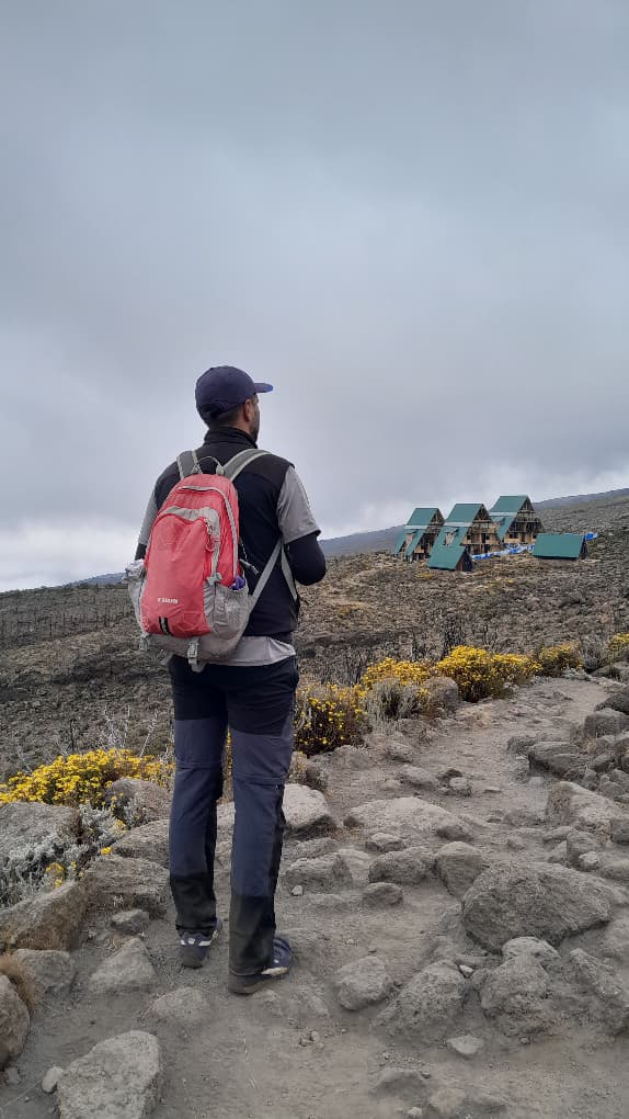 Trekker auf der Marangu-Route blickt über Landschaft mit Hütten im Hintergrund