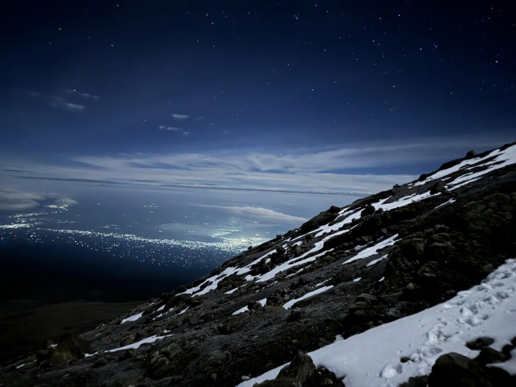 Blick vom Kilimanjaro hinunter ins Tal mit Wolkenmeer, Felsen und Schnee im Vordergrund