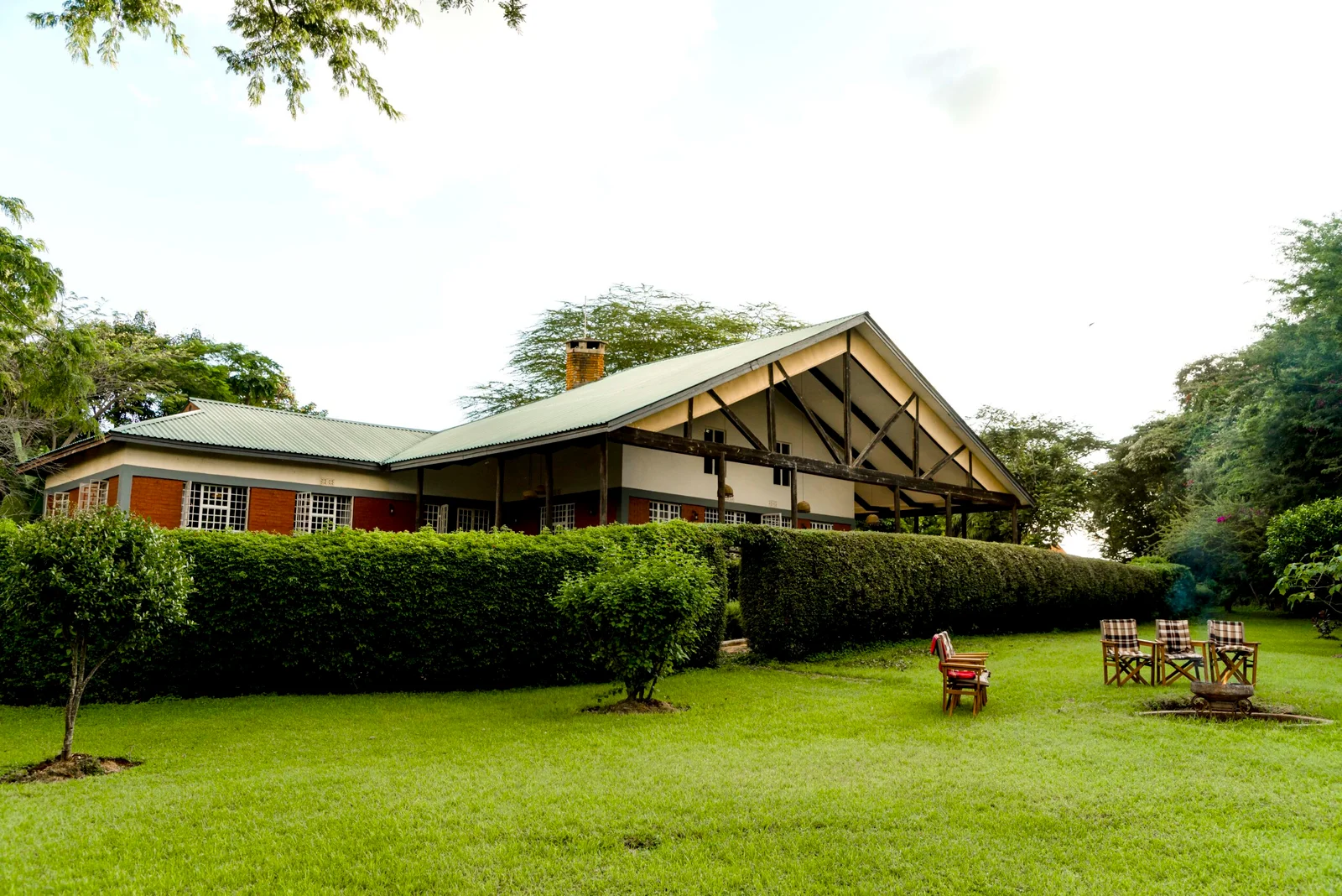 Gebäude der Olea Farm Lodge mit überdachter Terrasse, Rasenfläche und Gartenstühlen.