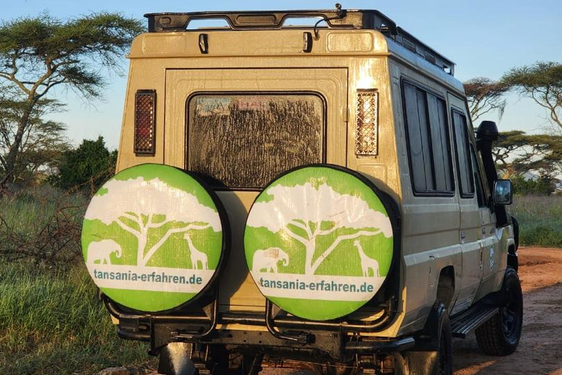 Safari-Geländewagen von hinten mit zwei Ersatzrädern und dem Logo von tansania-erfahren.de.