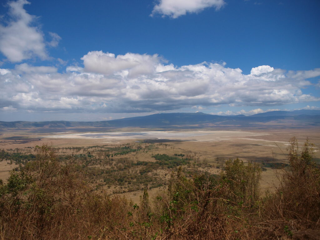 Weite Kraterlandschaft in Tansania mit einem See unter wolkigem Himmel.