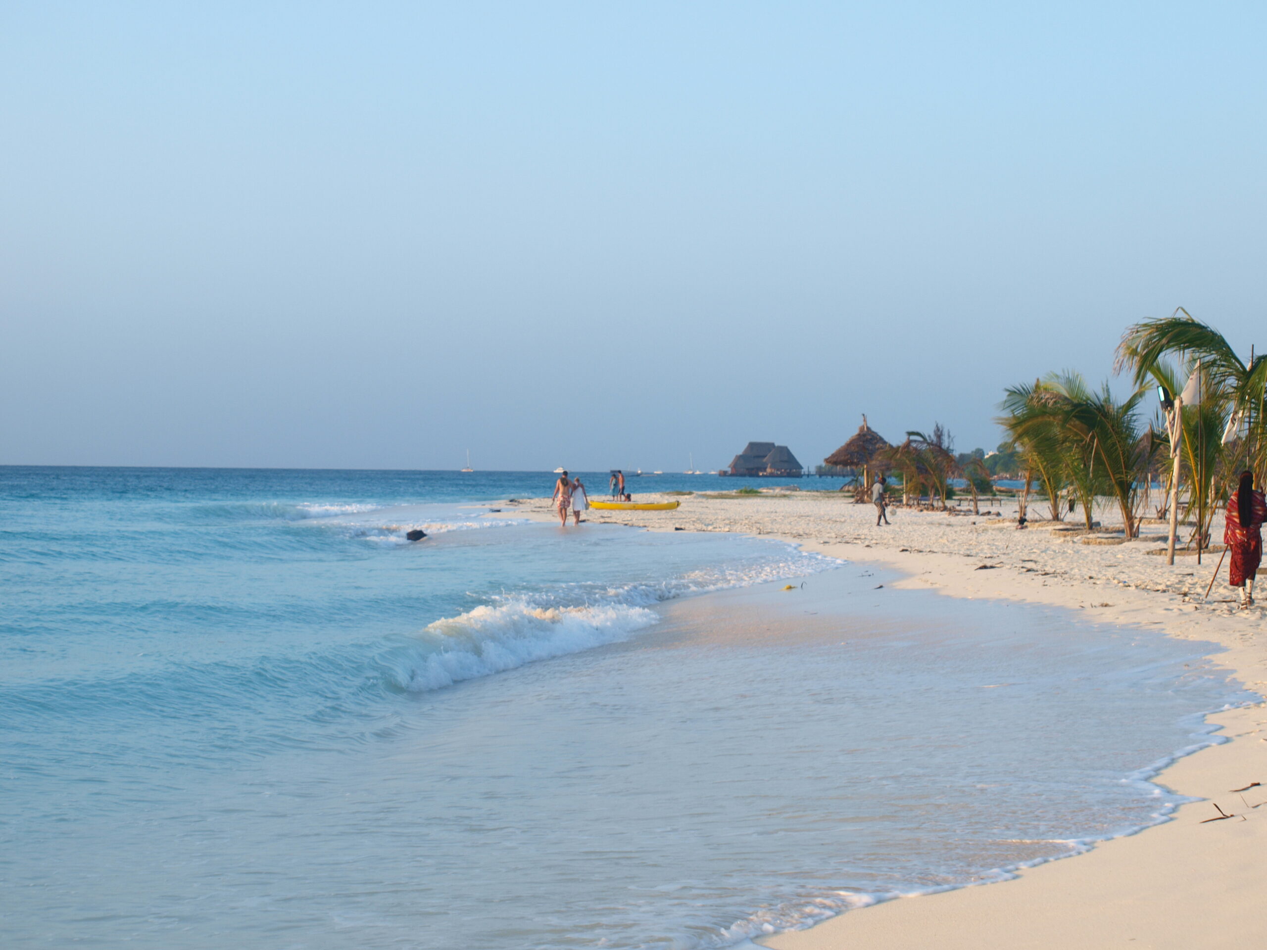 Sandstrand auf Sansibar mit Palmen, blauem Meer und Menschen am Ufer.